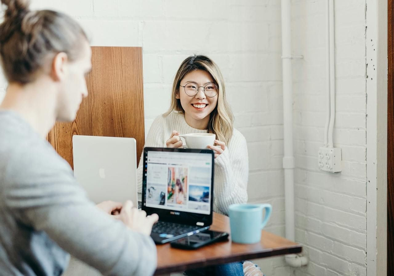 A man and woman are seated at a table, working together on a laptop.